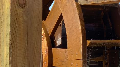 Wooden-wheel-of-watermill-turns-around,-water-splashing-on-paddles-close-up