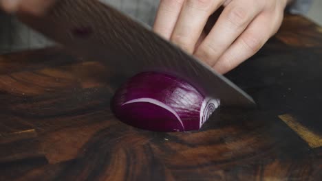 Slicing-onion-with-big-kitchen-knife-on-cut-board-in-home-kitchen