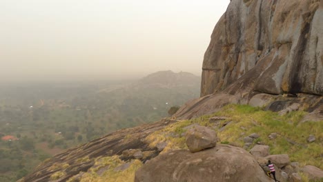 Aerial-shot-of-a-young-African-man-climbing-large-granite-boulders-on-a-mountain-in-Uganda