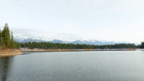 Timelapse-of-a-Smooth,-Empty-Lake-with-Snow-Covered-Mountains-in-the-Background-on-a-Beautiful-Sunny-Day,-Wide-Shot-with-Negative-Space