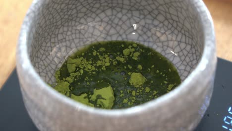 Extreme-close-up-shot-of-hot-water-added-into-ceramic-cup-with-matcha-powder,-preparation-of-ceremonial-matcha-tea