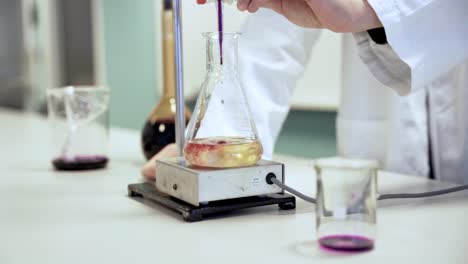 Slow-motion-shot-of-a-scientist-mixing-different-substances-in-a-glass,-wearing-a-white-jacket-in-a-lab