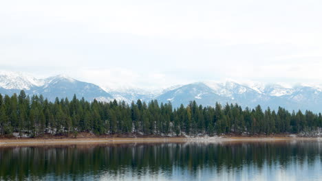 Timelapse-of-a-Calm,-Still-Lake-with-Evergreen-Trees-and-Snow-Covered-Mountains-in-the-Background,-Negative-Space