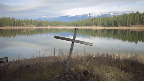 Ein-Einfaches-Holzkreuz-Am-Ufer-Eines-Wunderschönen-Sees-In-Den-Bergen-Von-Montana-An-Einem-Sonnigen-Tag,-Langsames-Einschieben
