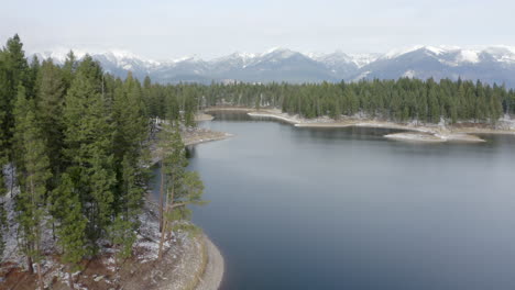 Aerial-Flyover-of-a-Remote-Lake-in-the-Wilderness-of-Montana-with-Snow-Covered-Mountains-in-the-Background