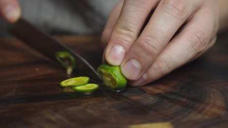Slicing-green-lime-lemon-with-kitchen-knife-on-wooden-cut-board