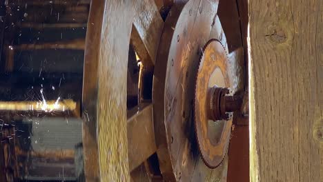 Wooden-wheel-of-water-mill-turns-around,-mechanism-with-spinning-cog-close-up