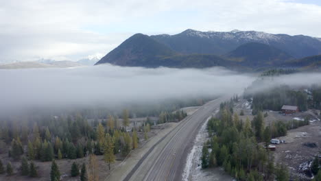 Drone-Shot-Rising-Above-an-Empty-Road-in-a-Foggy-Valley-with-the-Mountains-of-Montana-in-the-Background
