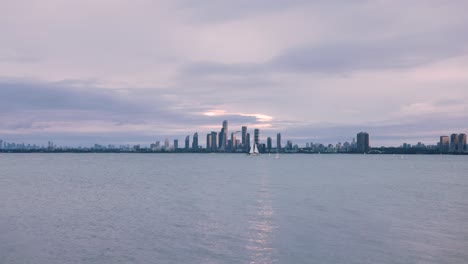 Waterfront-skyline-view-of-dense-urban-city-centre-with-high-rise-buildings-across-a-lake-at-sunset,-Toronto-Ontario