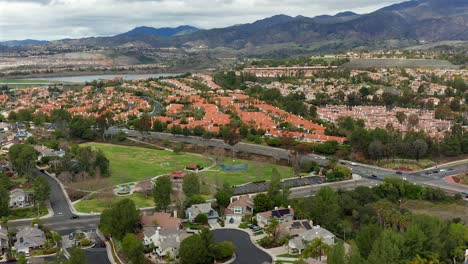 Aerial-view-in-Southern-California-of-a-park,-housing,-and-the-mountains,-on-an-overcast-day