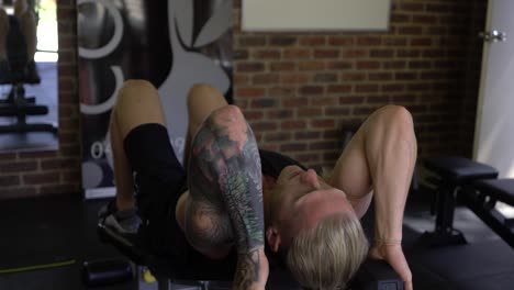 Tattoo-man-muscles-in-home-gym-doing-bench-tricep-skull-crusher-with-dumbbell