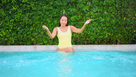 Smiling-young-asian-woman-is-playing-with-water-while-sitting-on-pool-border-on-hot-summer-day,-slow-motion