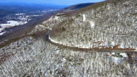 Aerial-drone-video-footage-of-a-snowy,-blue-sky-mountain-valley-road-highway-through-the-mountains-in-the-Appalachians-on-the-Shawangunk-ridge,-in-new-York-state
