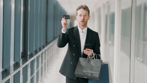 Stylish-business-man-with-paper-bags-shows-a-credit-card