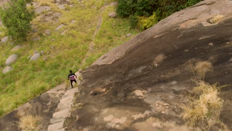 Aerial-shot-birds-eye-view-of-an-African-man-walking-down-stairs-on-the-side-of-a-granite-mountain