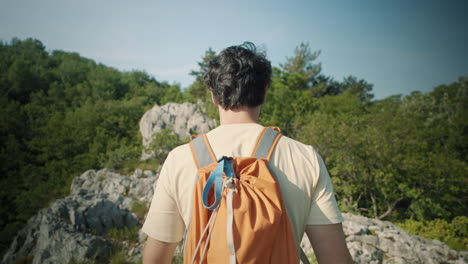 Camera-tracking-a-hiker-with-an-orange-backpack-from-behind-on-a-rocky-path-on-mountain-Sabotin