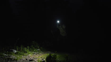Hiker-walking-up-a-mountain-in-pith-black-just-before-the-dawn,-illuminating-his-path-with-a-headtorch