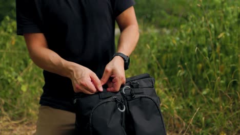 Hands-opening-up-a-backpack-and-removing-items-from-top-of-bag-outdoors-in-natural-landscape