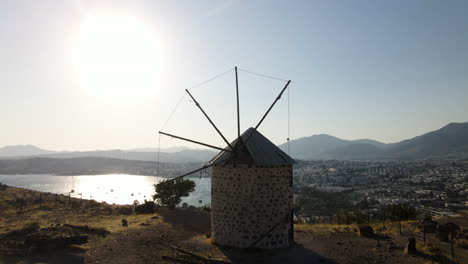 Aerial-shot-of-an-old-windmill-on-the-top-of-a-mountain-with-a-city-in-the-background