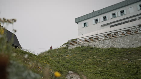 Low-perspective-of-a-hiker-walking-in-a-distance-towards-the-benches-in-front-a-mountain-cottage-on-mountain-Črna-prst