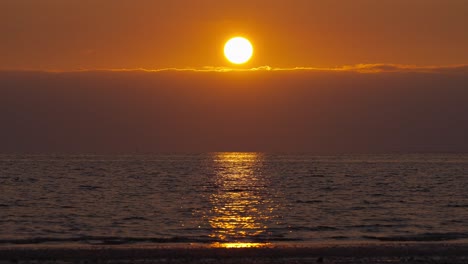 Slowmotion-shot-of-a-vibrant-sunset-setting-over-the-ocean-on-the-horizon