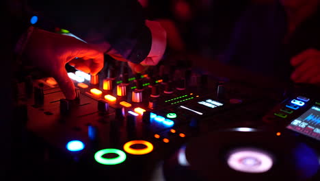The-DJ-at-his-mixer-table-at-the-nightclub-turning-the-knobs-and-pushing-buttons-with-flashing-lights