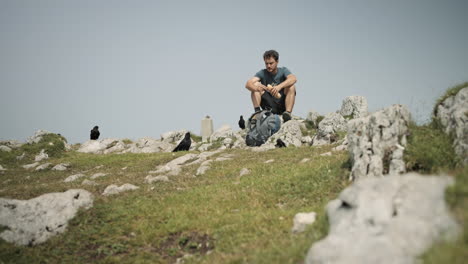 Alpine-choughs-surrounding-hiker-who-is-sitting-on-the-rock-and-eating-his-sandwich-at-the-top-of-mountain-Raduha