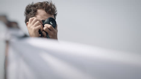 Man-taking-a-picture-with-his-camera,-white-fabric-fluttering-in-foreground