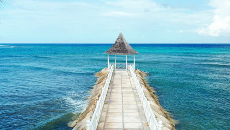 Tropical-beach-view-of-broad-walk-leading-to-gazebo-surrounded-by-turquoise-Caribbean-ocean