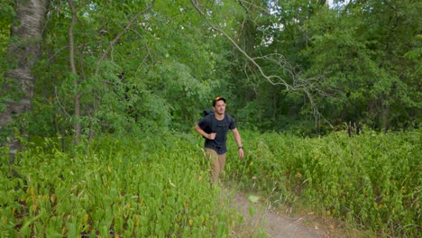 modern-male-hiker-in-summer-emerges-from-forest-and-walks-down-trail-towards-camera