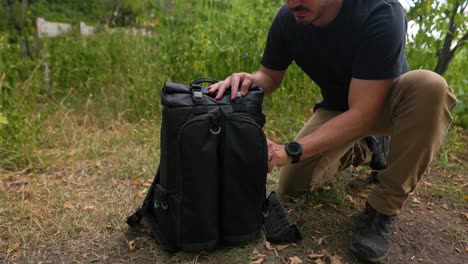 Male-photographer-reaches-into-camera-bag-pulls-out-drone-photography-equipment-outdoors-in-a-forest-setting