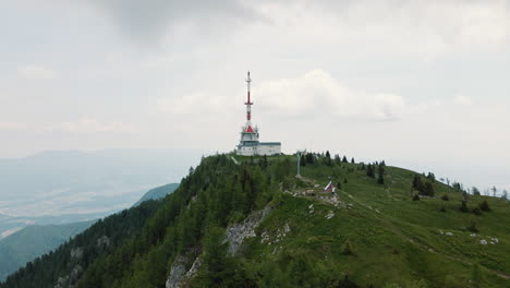 Pan-drone-shot-of-a-top-of-mountain-Uršlja-gora-with-a-radio-tower,-covered-with-shadows-from-clouds-above