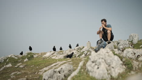 Man-sitting-on-the-rock-eating-his-sandwich,-low-perspective,-birds-surrounding-him-and-waiting-for-some-shared-food