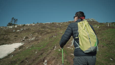 Camera-tracking-a-male-hiker-with-a-light-green-backpack-and-green-hiking-poles-on-a-uphill-path-on-the-mountain-Ratitovec