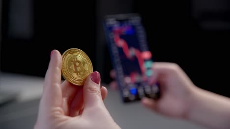 Female-fingers-holding-golden-bitcoin-watching-crypto-trading-investment-chart-decline-on-smartphone
