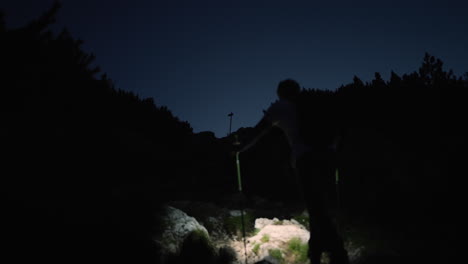Camera-shot-from-behind-of-a-hiker-climbing-up-a-mountain-with-his-headtorch-to-illuminate-his-path-towards-the-top
