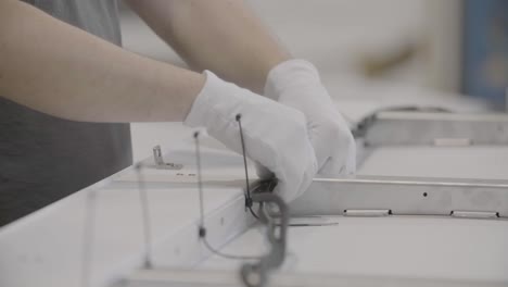 Close-up-of-two-hands-in-white-gloves-carefully-connecting-a-wire-to-a-board-using-cable-ties-in-a-documentary-style-handheld-shot,-all-in-focus