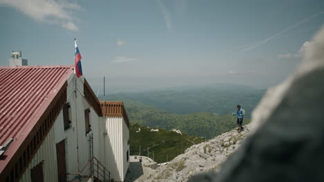 Hiker-walkig-from-behind-the-rock-towards-the-cottage-on-mountain-Snežnik