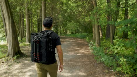 Photographer-hiking-through-dense-green-forest-with-modern-camera-backpack-and-tripod-gear