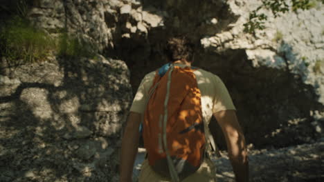 Hiker-with-an-orange-backpack-wearing-summer-clothes-walkig-towards-the-tunnel-carved-into-the-rock-and-entering