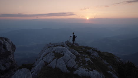 Hiker-standing-at-the-edhe-of-a-mountain-ridge-to-admire-the-early-morning-vive-and-the-sunrise