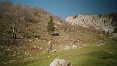 Excursionista-Caminando-Con-Bastones-De-Senderismo-En-Una-Colina-En-Una-Montaña-En-Primavera,-árboles-Caducos-Todavía-Sin-Hojas,-Cielo-Azul-Claro