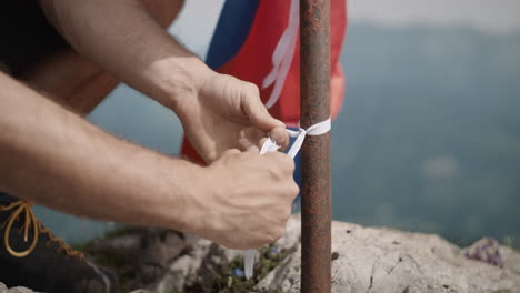 Man-tieing-slovenian-flag-to-the-pole-to-let-if-flutter-at-the-top-of-mountain