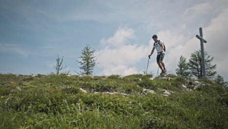 Young-hiker-with-hiking-poles-walking-at-the-top-of-the-ridge,-camera-shot-with-a-low-perspective,-past-the-wooden-bech-with-a-carved-heart-in-the-middle