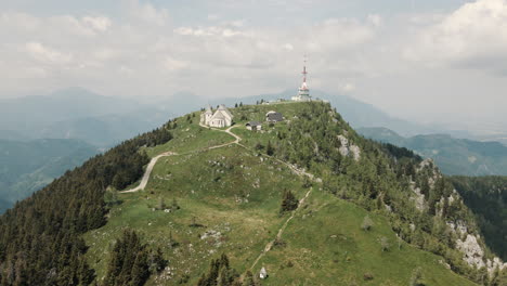 Drohnenaufnahme-Des-Berges-Uršlja-Gora,-Sonnen-Sich-In-Sonne,-Wolken-Und-Tal-Im-Hintergrund