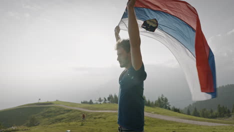Junger-Mann,-Der-In-Seinen-Armen-über-Seinem-Kopf-Eine-Slowenische-Flagge-Hält,-Lässt-Sie-Im-Wind-Flattern