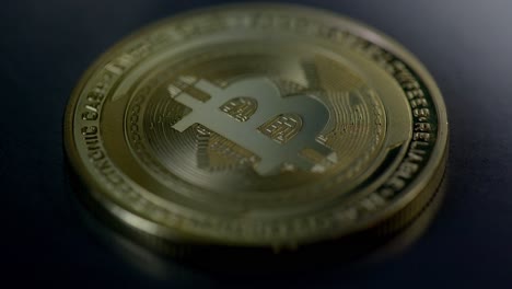 A-physical-golden-Bitcoin-coin-lying-on-the-dark-table-with-a-shadow-sweep---macro-shot