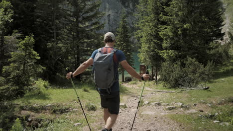 Hiker-walking-towards-the-Krn-lake-with-hiking-poles-and-a-backpack-on-his-shoulders,-conifers-covering-the-view-of-lake