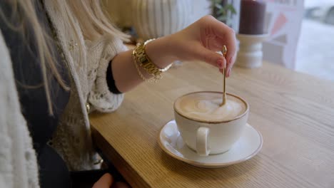Female-slowly-stirring-cup-of-coffee-with-golden-spoon-in-cafe