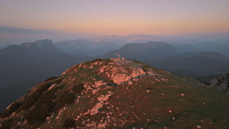 Toma-De-Drone-De-La-Cima-De-La-Montaña-Peca-En-El-Sunrse-Donde-Un-Excursionista-Sostiene-Una-Bandera-Eslovena-En-El-Poste